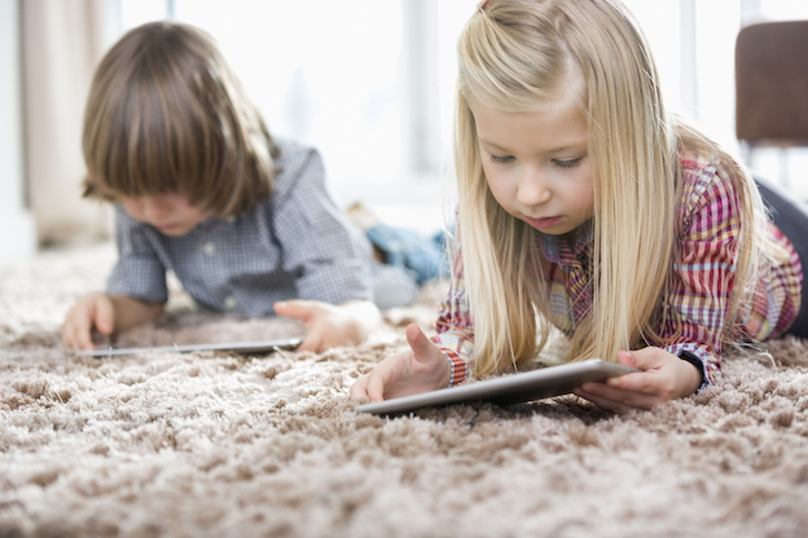 Cute girl and brother using digital tablets on rug in living room
