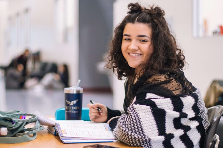 college student at a table smiling.