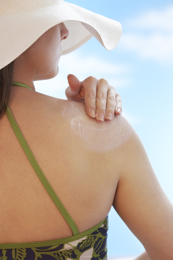Woman applying sunscreen to shoulder back view