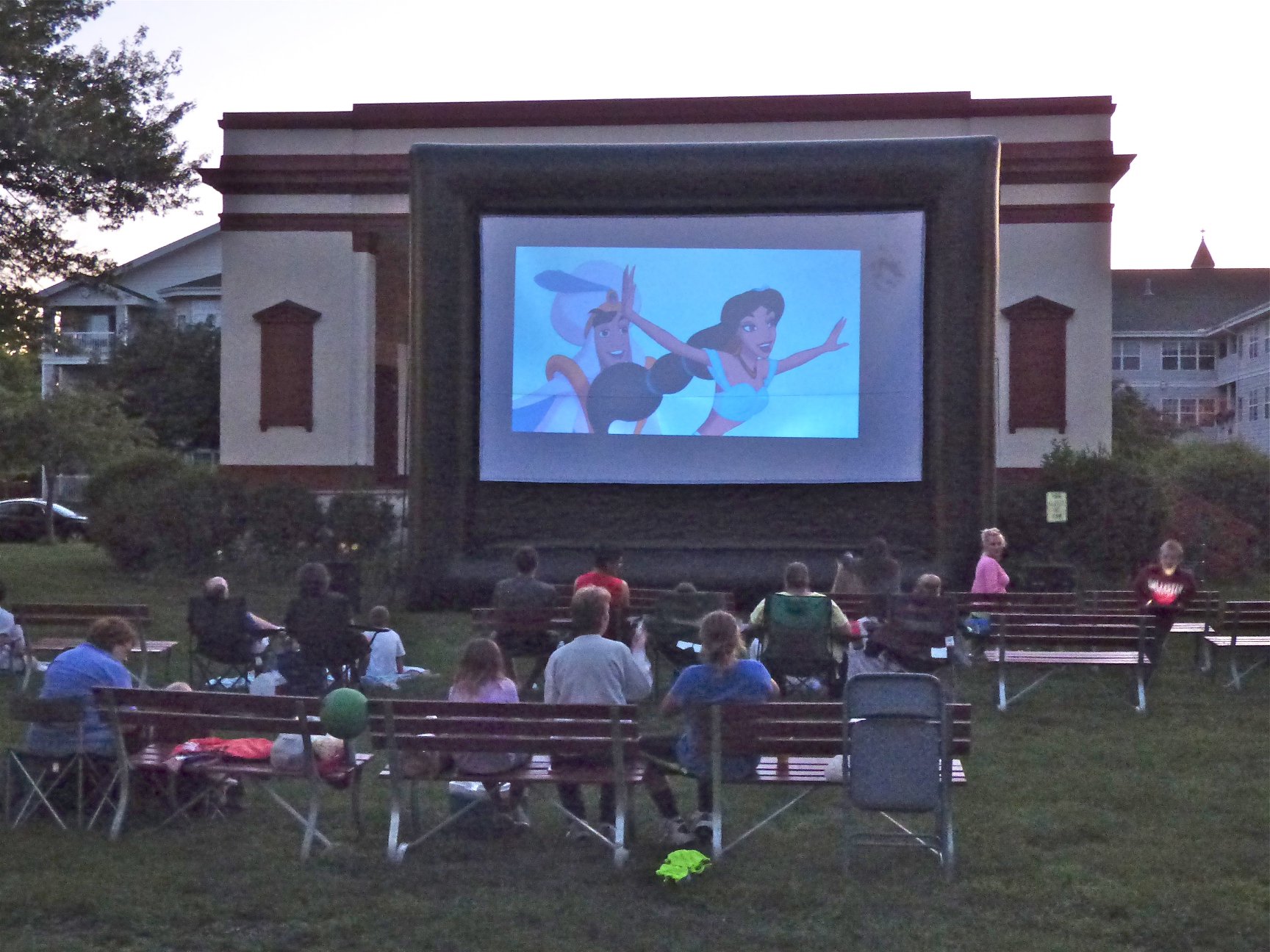 people watching Aladdin in park on large movie screen