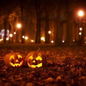 two carved jack-o-lanterns in field at night