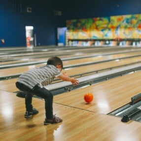 Kid bowling with orange ball.