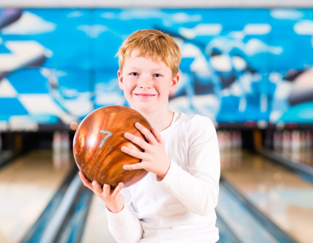 boy at bowling alley holding orange bowling ball