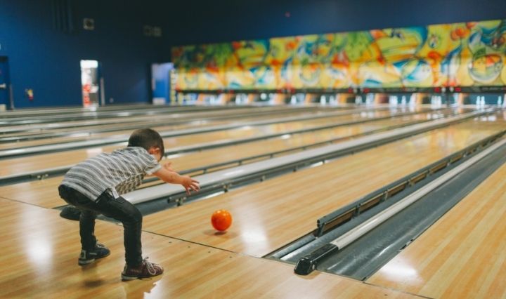 child bowling with orange bowling ball.