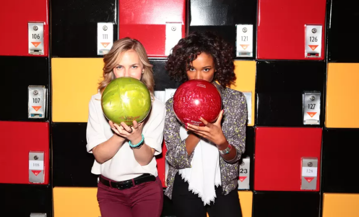 two women holding bowling balls in front of lockers