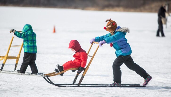 kids pushes sleds on snow.