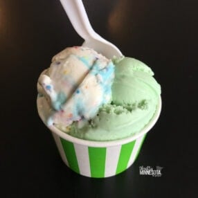 Pistachio and Birthday Cake Ice Cream in Green Striped Cup with plastic spoon.