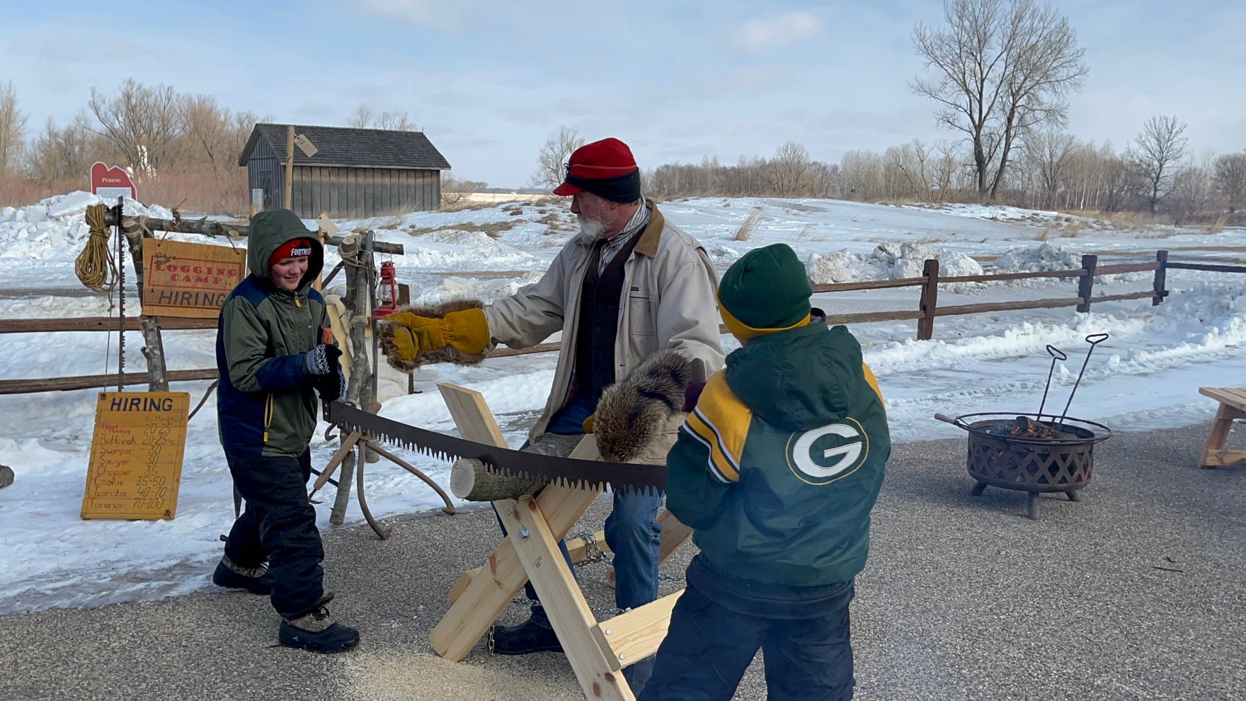 Boys sawing log with 2-person saw with older man supervising.