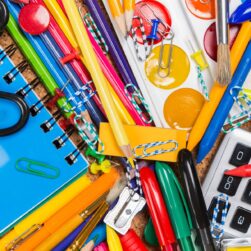 pile of school supplies with pencils, markers, paint, calculator, notebook.