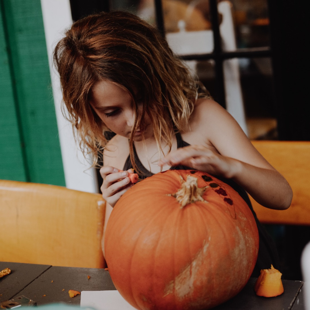 Girl carving pumpkin with tool.