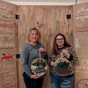 Two women posing with their holiday crafts at Christmas Craft Night.