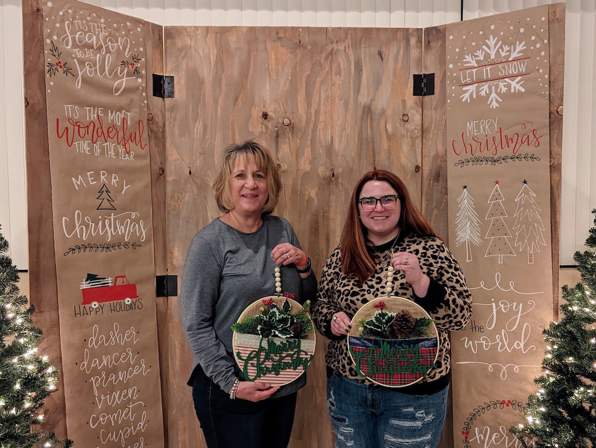 Two women posing with their holiday crafts at Christmas Craft Night. 