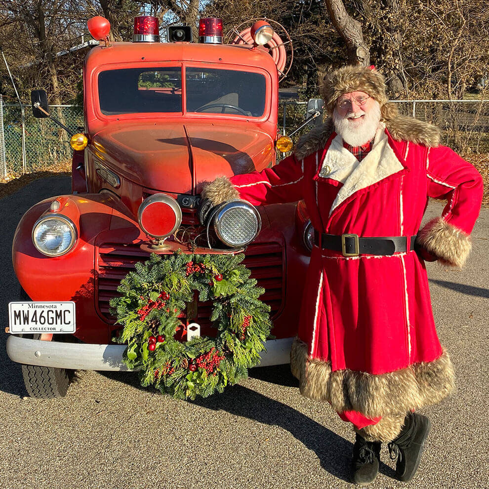 Santa standing in front of a small fire truck.