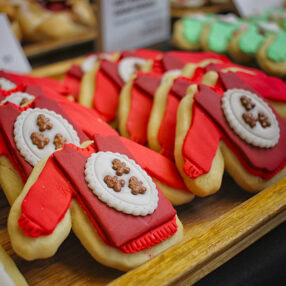 Close-up of festive cookies shaped like red sweaters with white and brown icing decorations, arranged on a wooden tray.