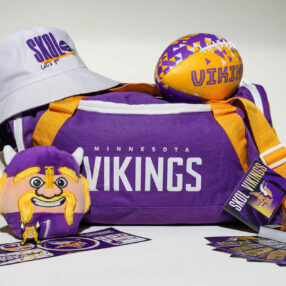 A Minnesota Vikings merchandise collection including a purple and white duffel bag, cap, plush toy, mini football, keychain, fan cards, and stickers, all featuring the team's logo and colors.