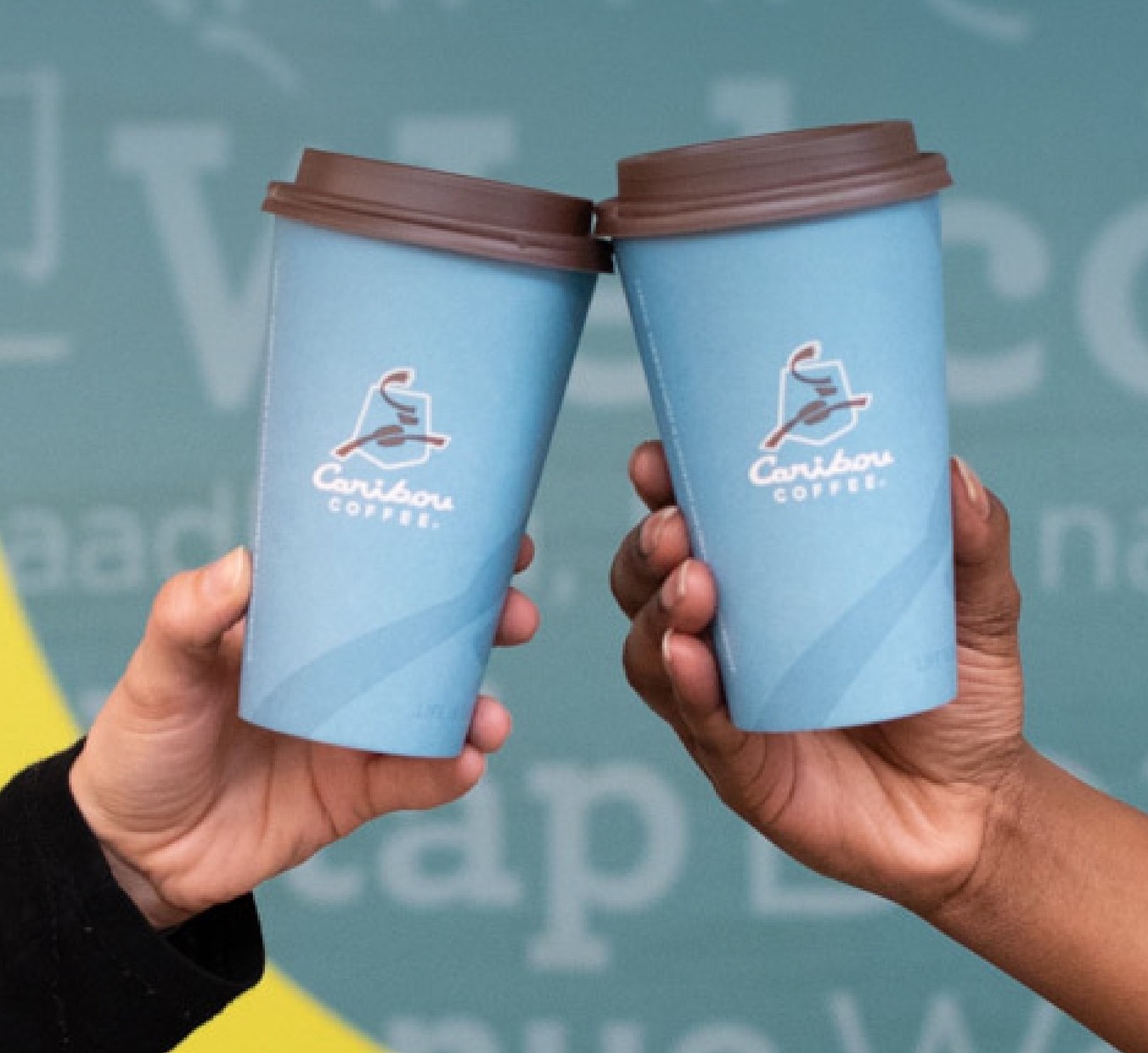 Hands of two people making a toast with Caribou Coffee disposable cups.