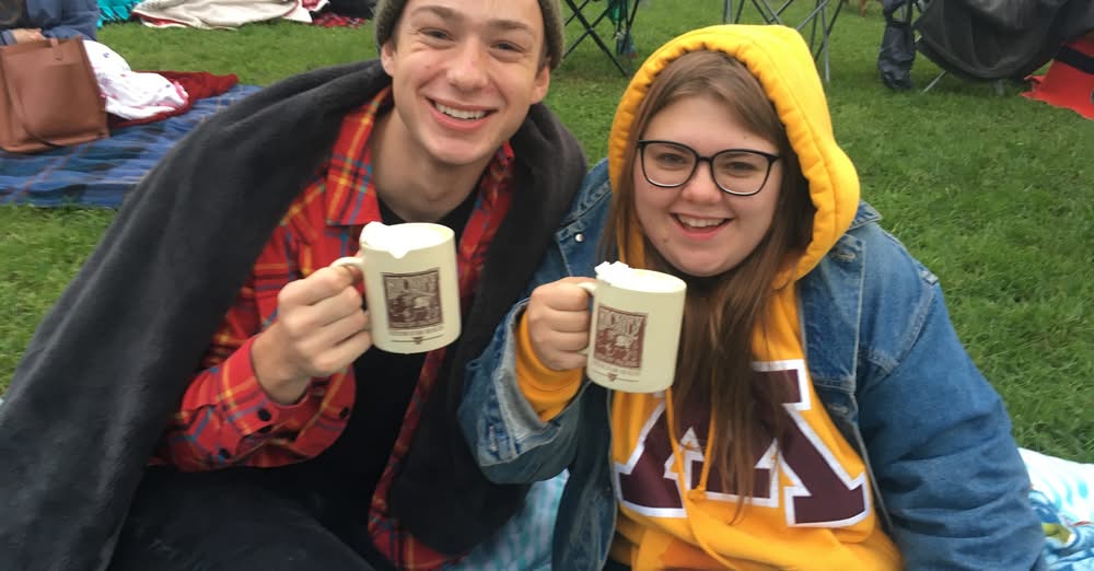 Couple attending St Paul Scary Movies in the park event wearing warm clothing and holding mubs of hot chocolate.