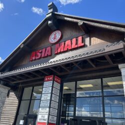 Entrance of Asia Mall with a wooden facade and a bright red sign. A directory board lists various shops inside. The sky is clear and blue, enhancing the rustic look of the mall's exterior.