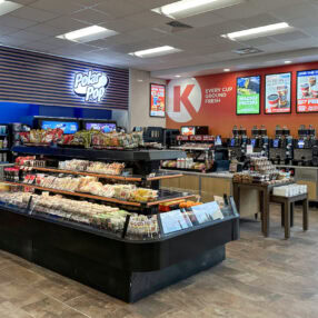 Holiday Stationstore interior with displays of snacks, sandwiches, and beverages. The store features a self-serve coffee and soda station, digital screen menus, and an ATM. Brightly lit and organized for easy access.