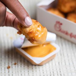 Chick-fil-A nugget up close with hand dipping into sauce.